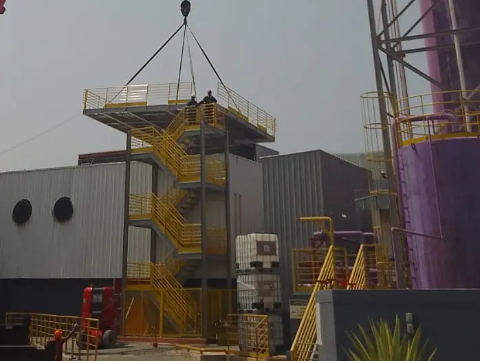 Escada metálica industrial amarela com patamares e guarda-corpo de acesso a plataforma externa